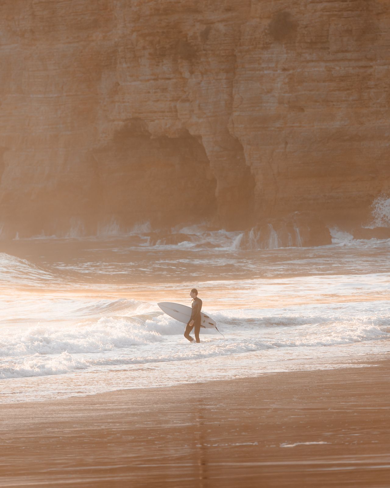 Figure walking a wide beach beneath golden cliffs