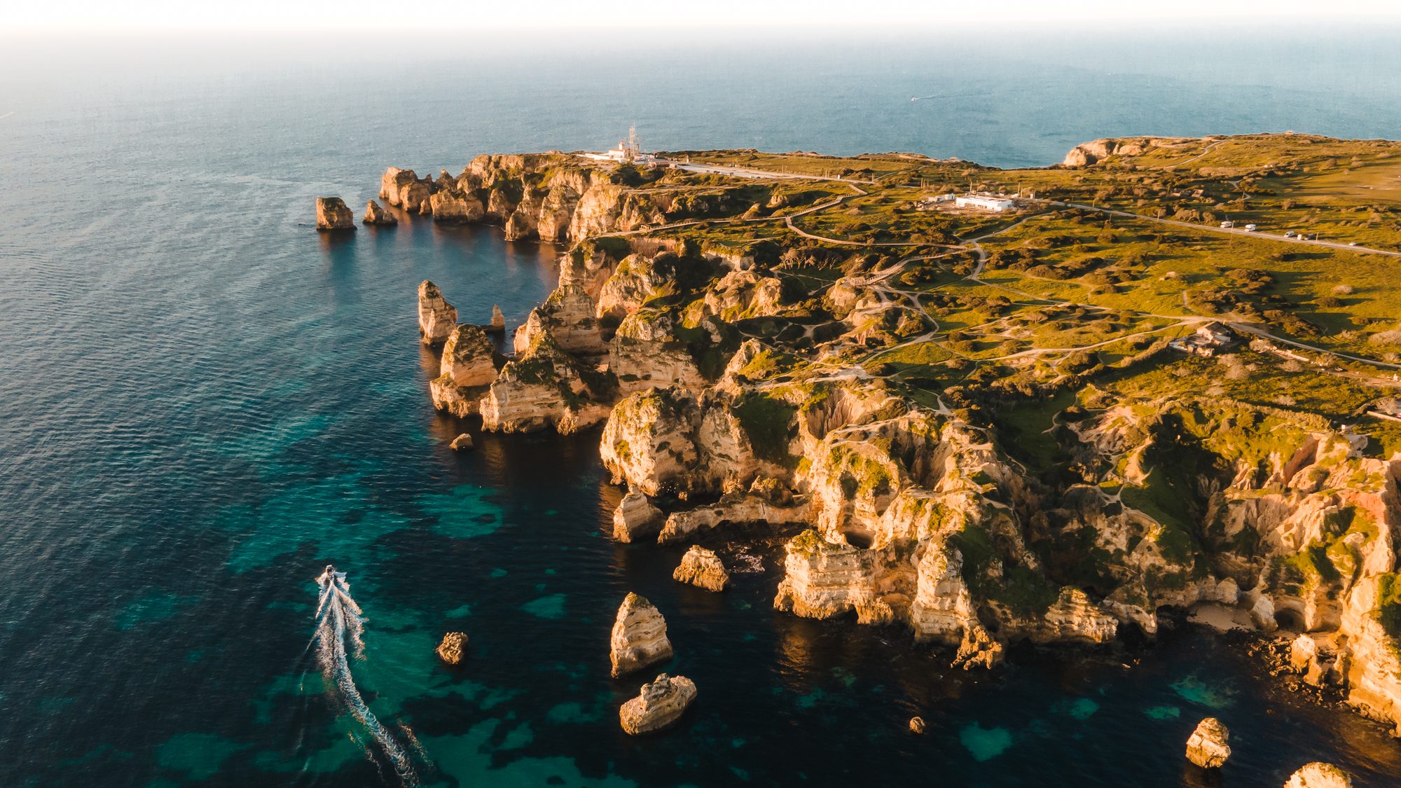 Aerial view of limestone cliffs, a lighthouse and turquoise water on the Algarve coast