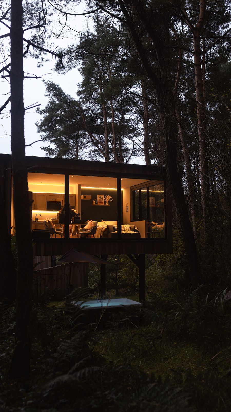 Warm interior seen through full height glazing from the forest