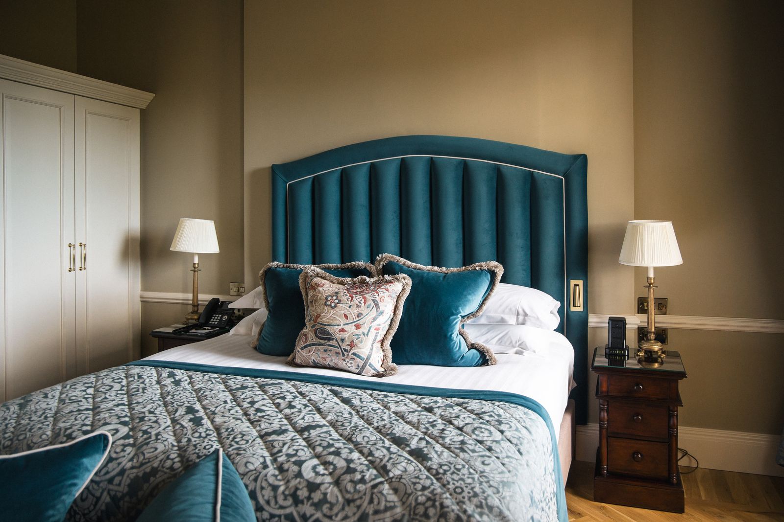 Suite bedroom with a deep teal velvet headboard at Castlemartyr