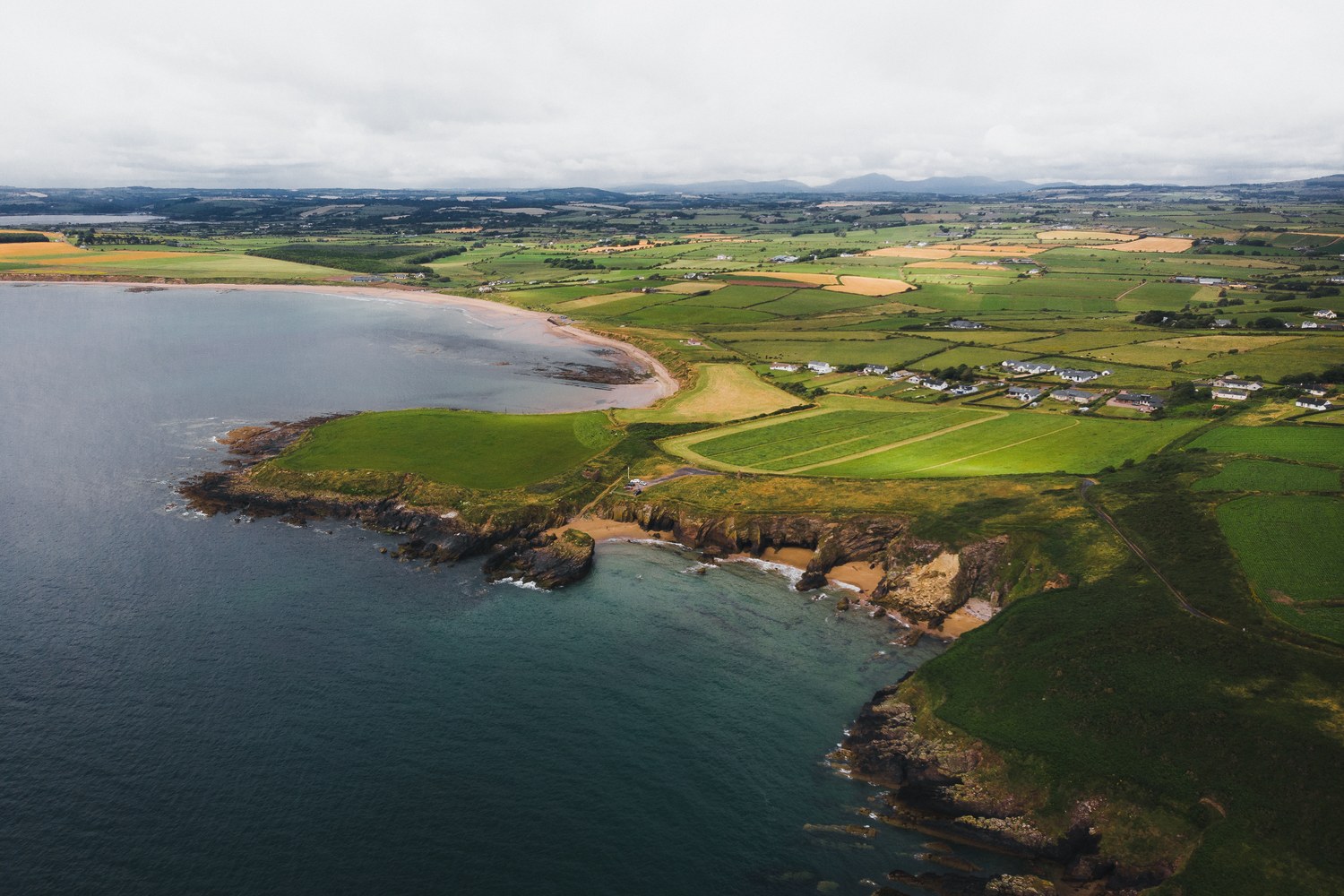 Green fields meeting a turquoise bay, seen from above