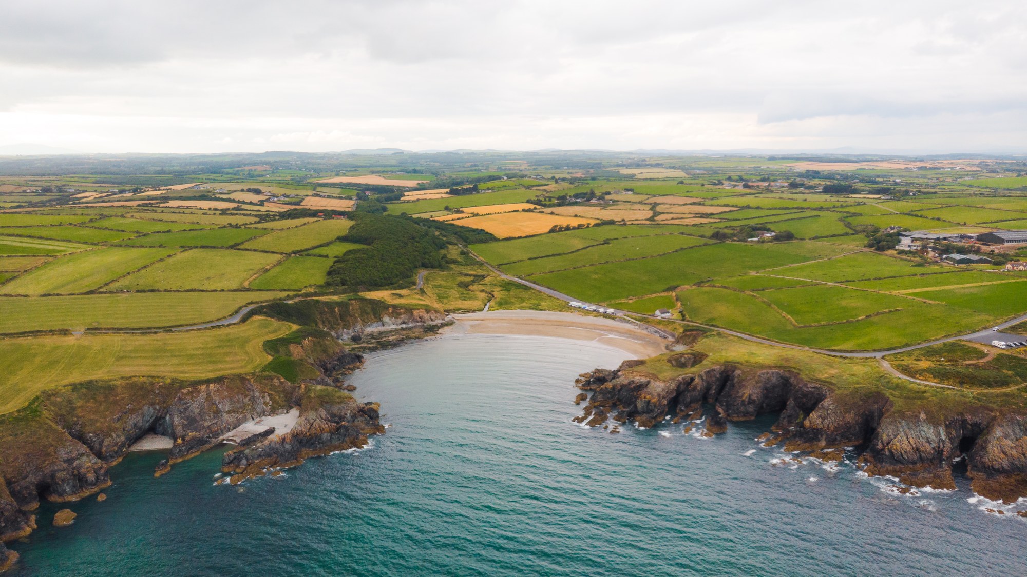 Aerial view of a sandy cove cut into farmland and cliffs