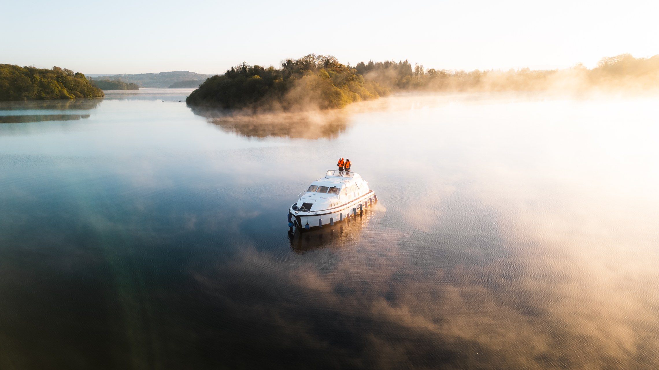 A cabin cruiser moving through golden mist on a wide lake