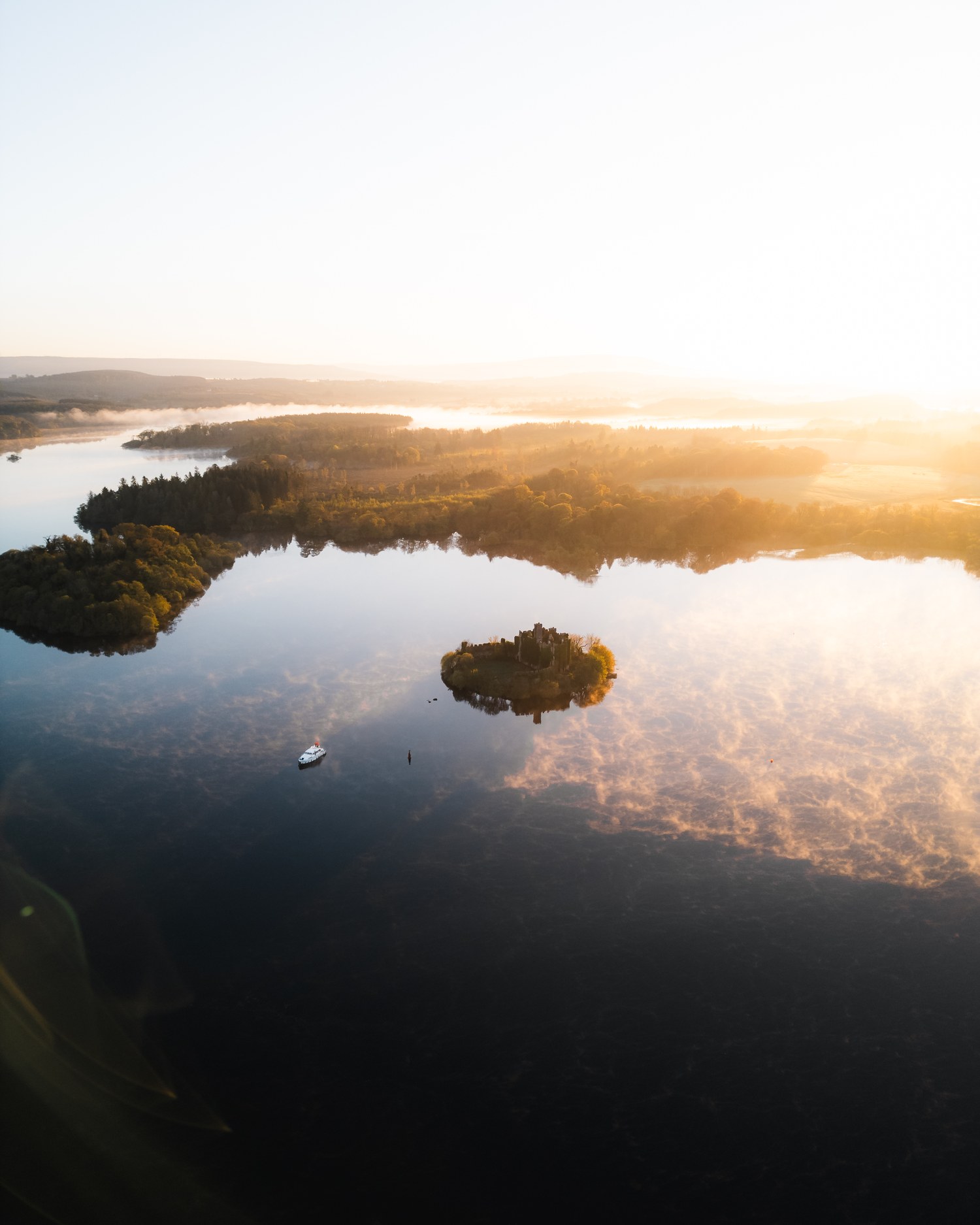 Low sun burning through mist over a wooded island