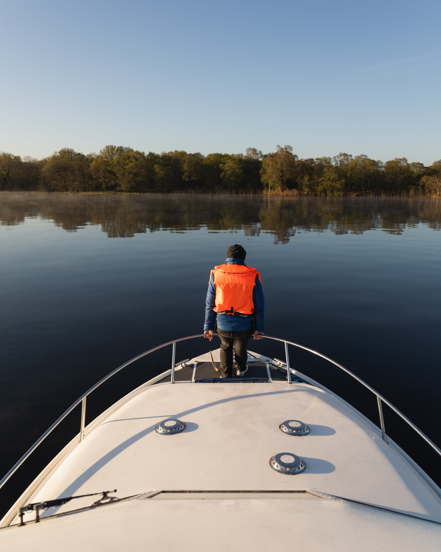 A traveller on the bow of a boat, looking down the lake