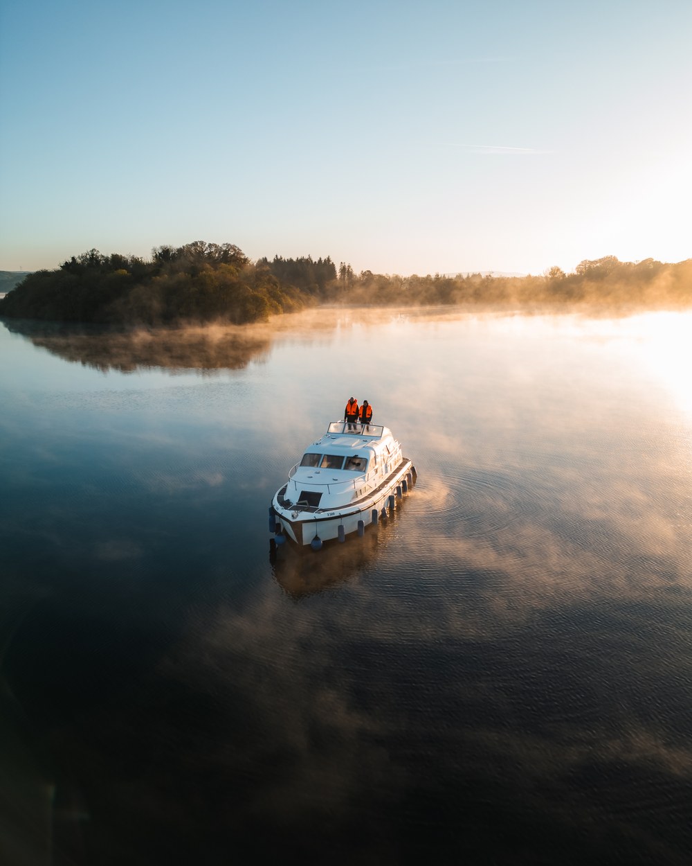 Two people standing on a cabin cruiser in golden morning mist