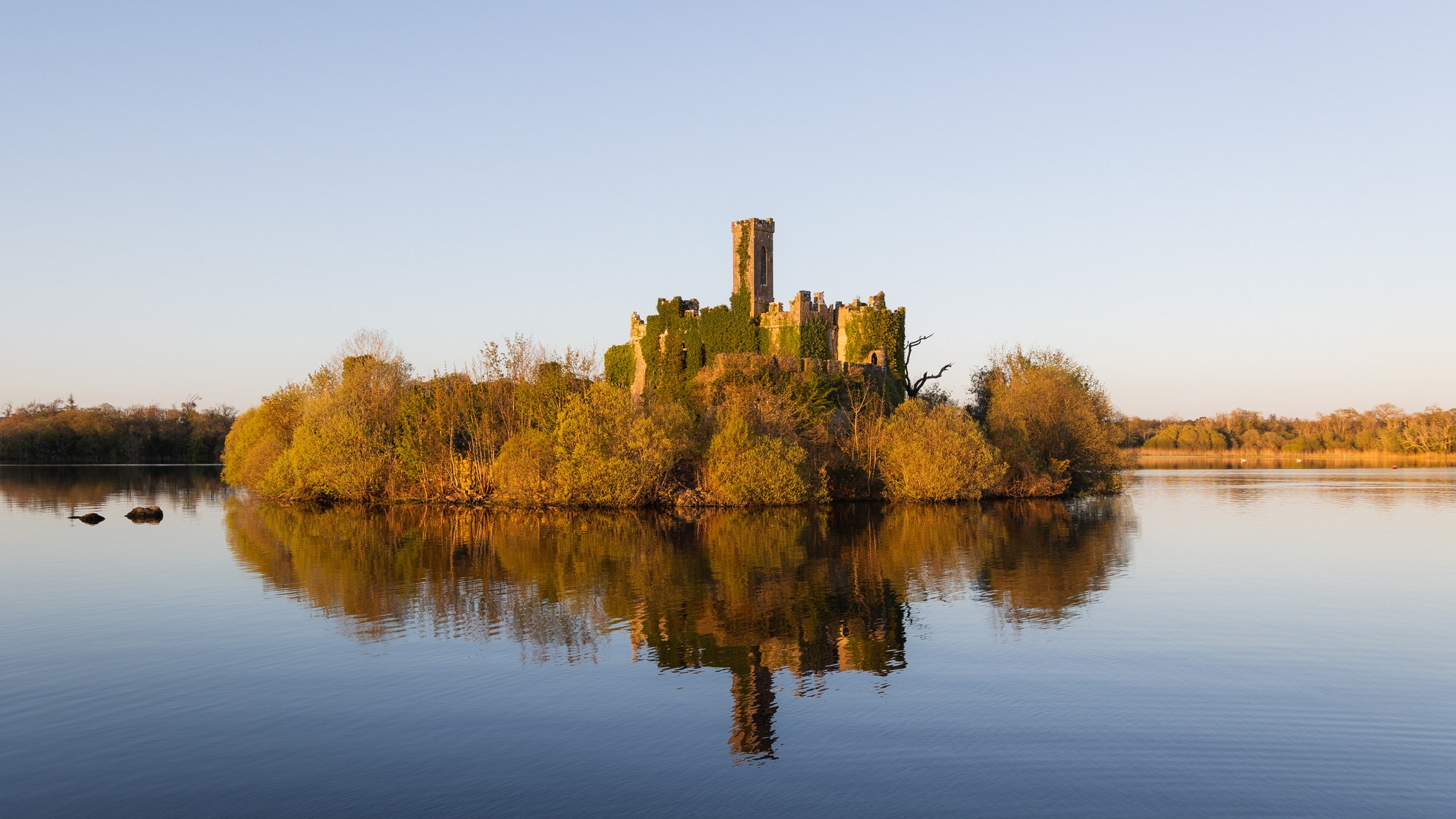 An island castle mirrored in still lake water at dawn