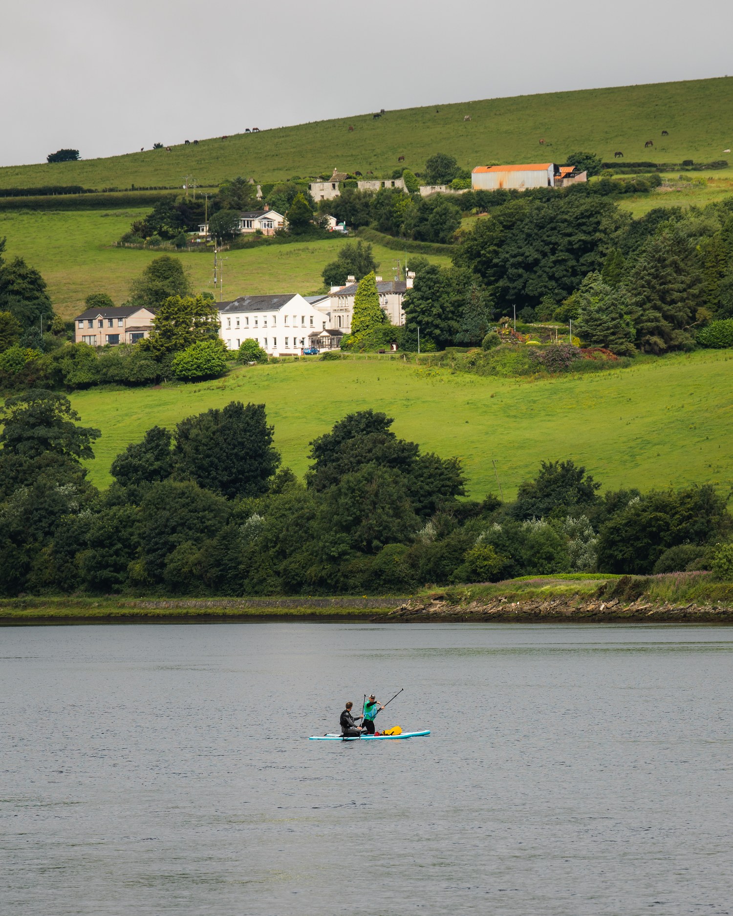 Two people kayaking on a lake below a country house