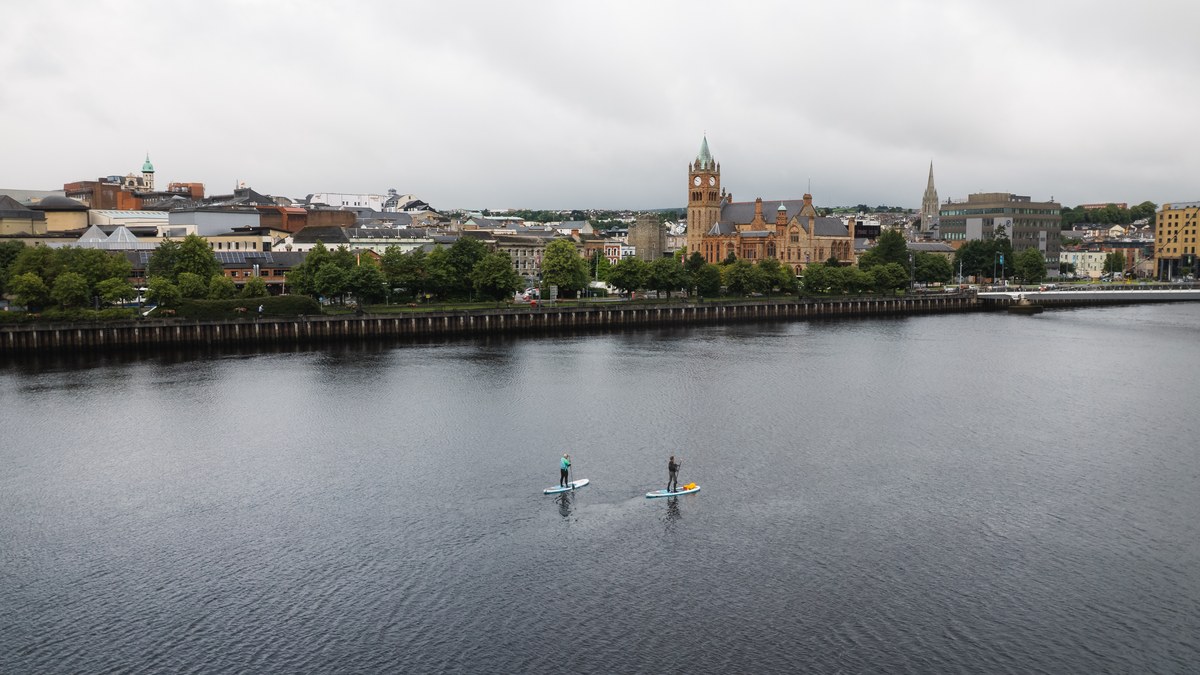 A riverside city seen across the water, paddleboarders in the foreground