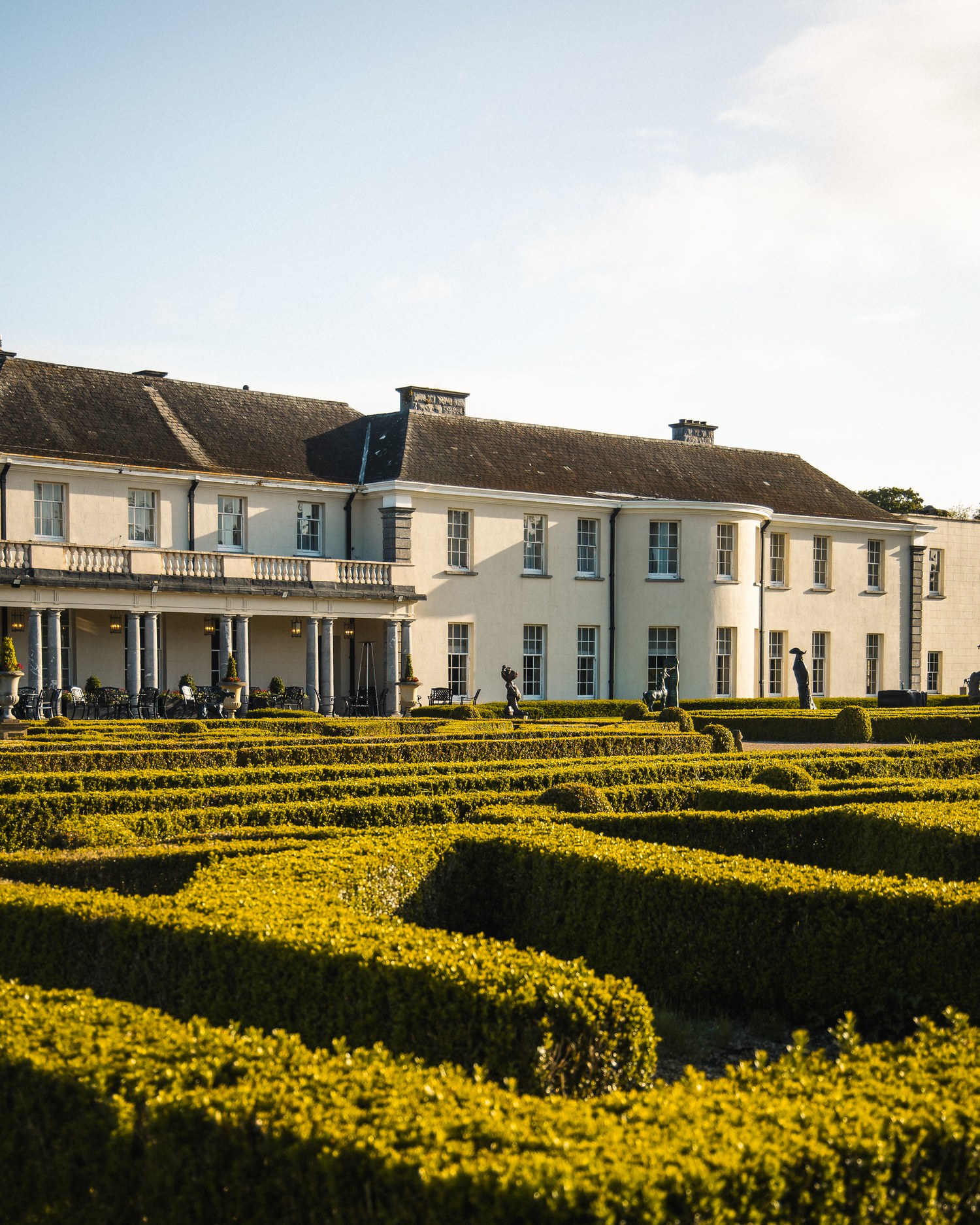 A formal garden and clipped hedges beside a country house, seen from above
