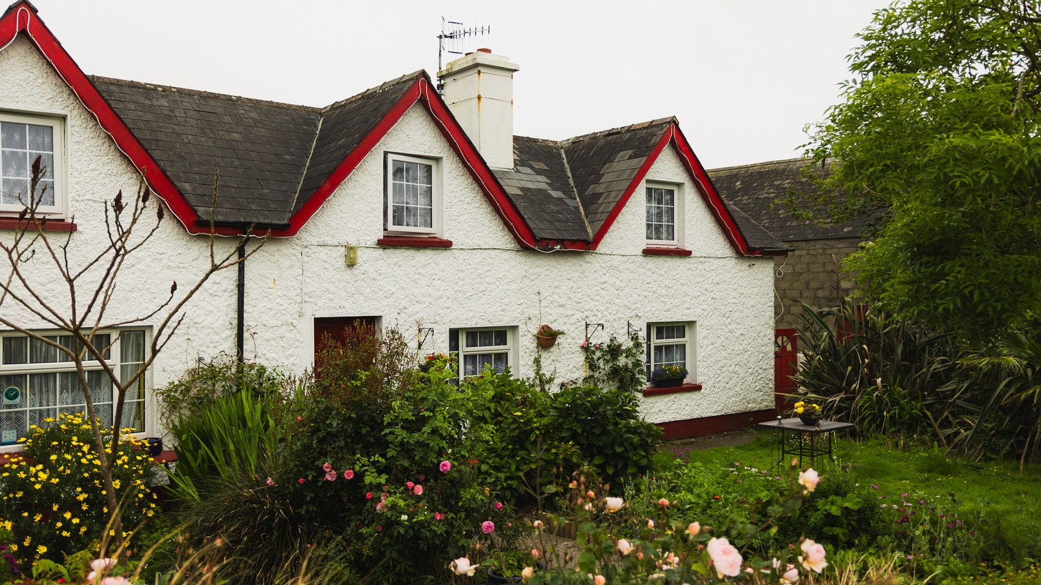 A red roofed cottage behind a flowering garden