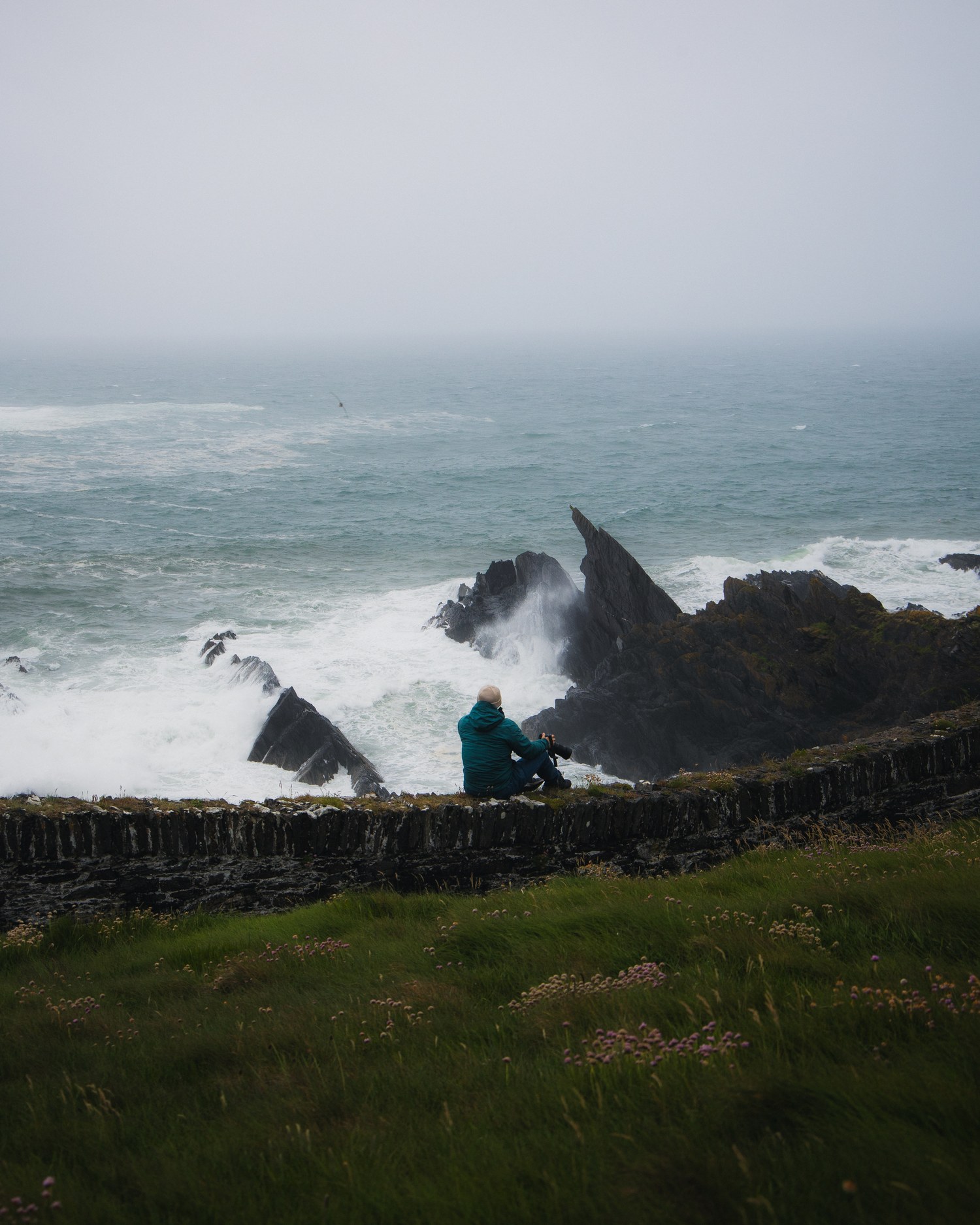 A walker seated on a stone wall above rough Atlantic surf