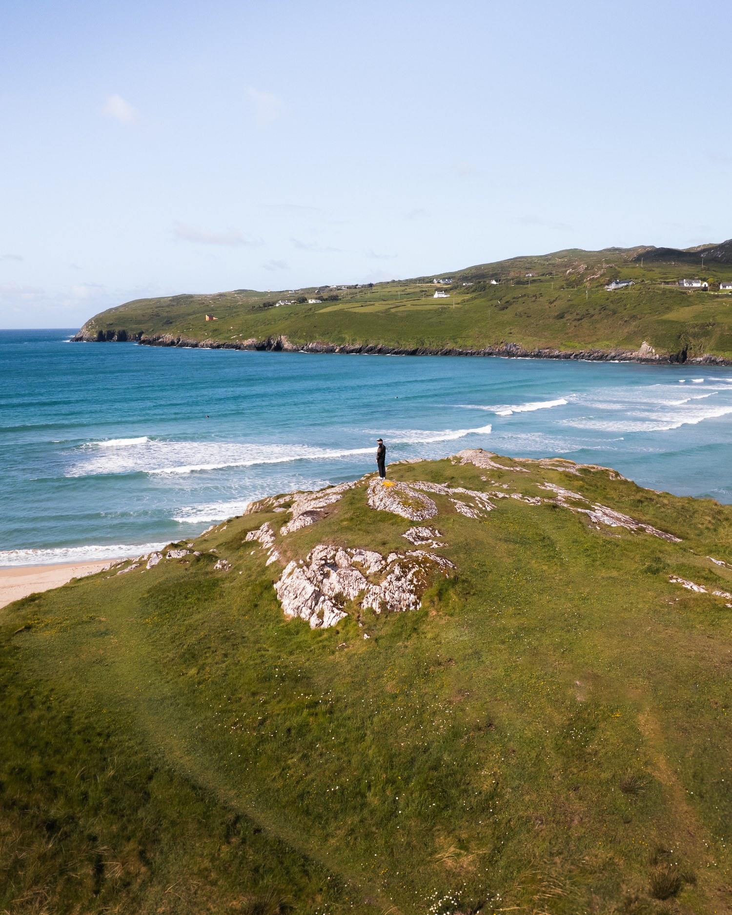 A walker standing at the edge of a grassy clifftop above a cove