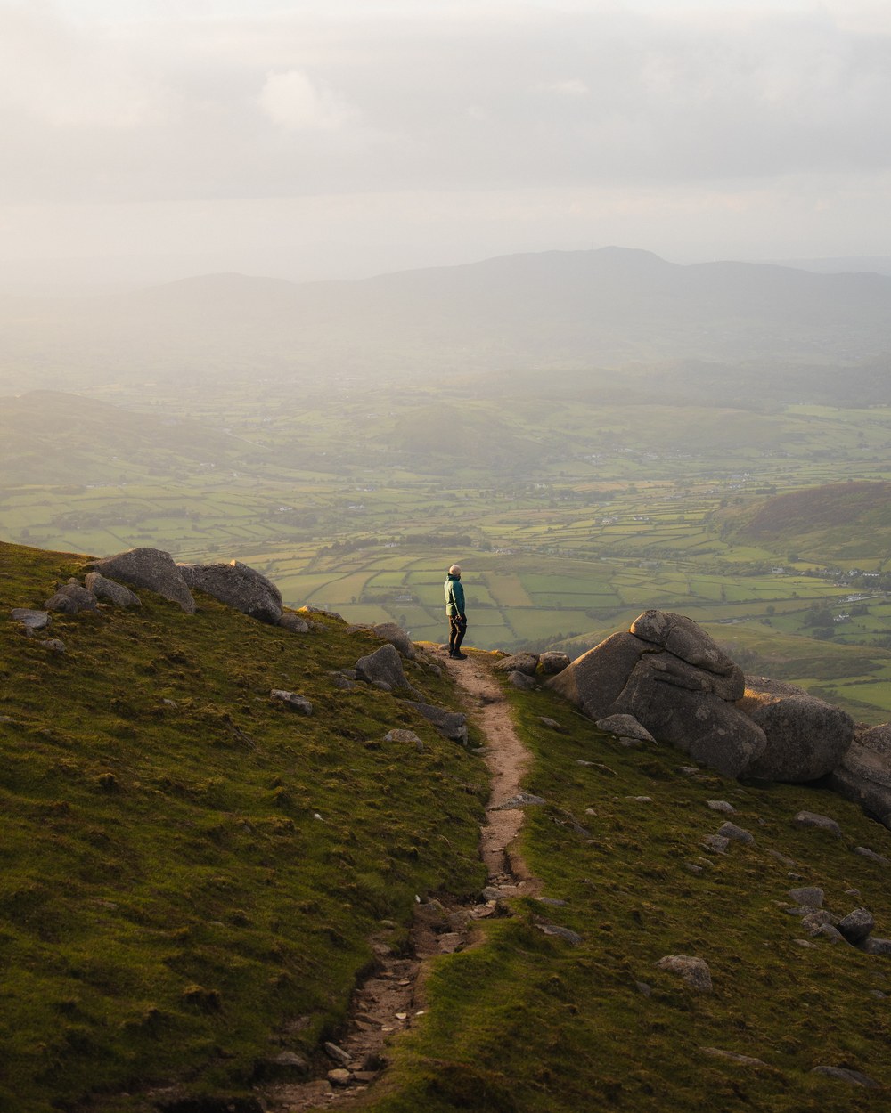A walker on a mountain path above a wide green valley