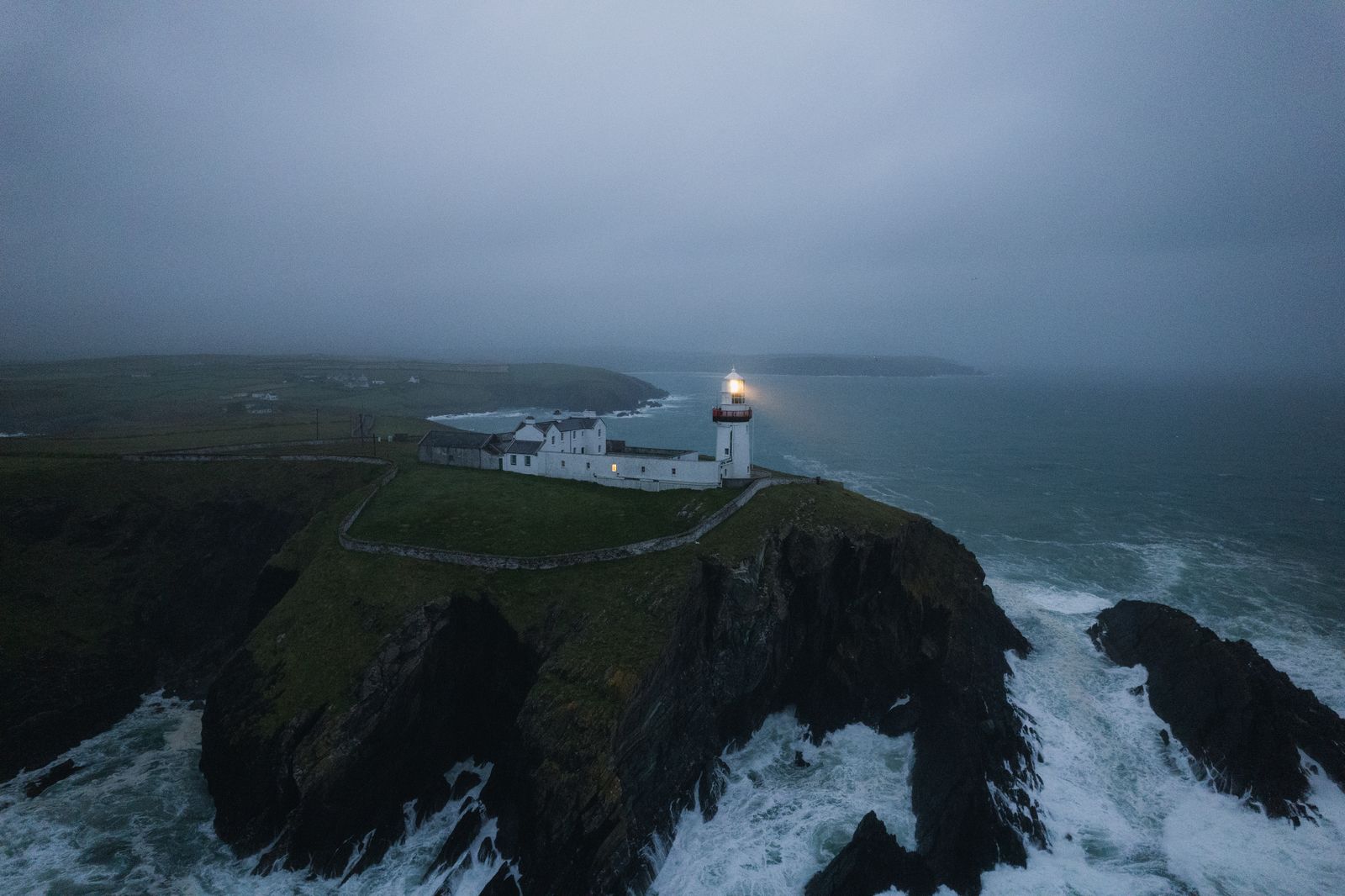 Lighthouse on dark cliffs with sea mist rolling in