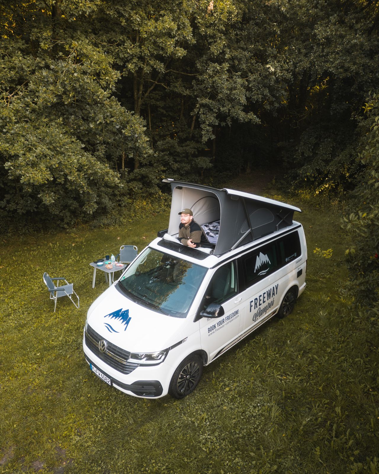 Van parked among trees with a traveller sitting outside