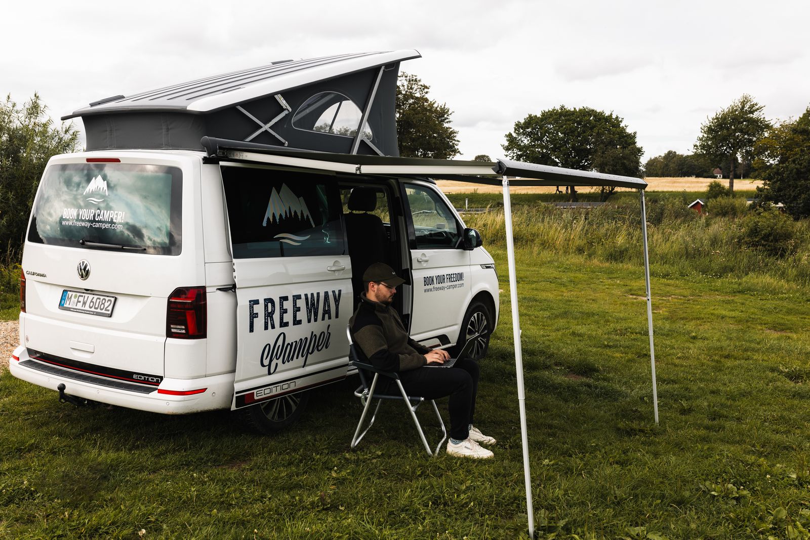 Van with awning out on grass beside the water