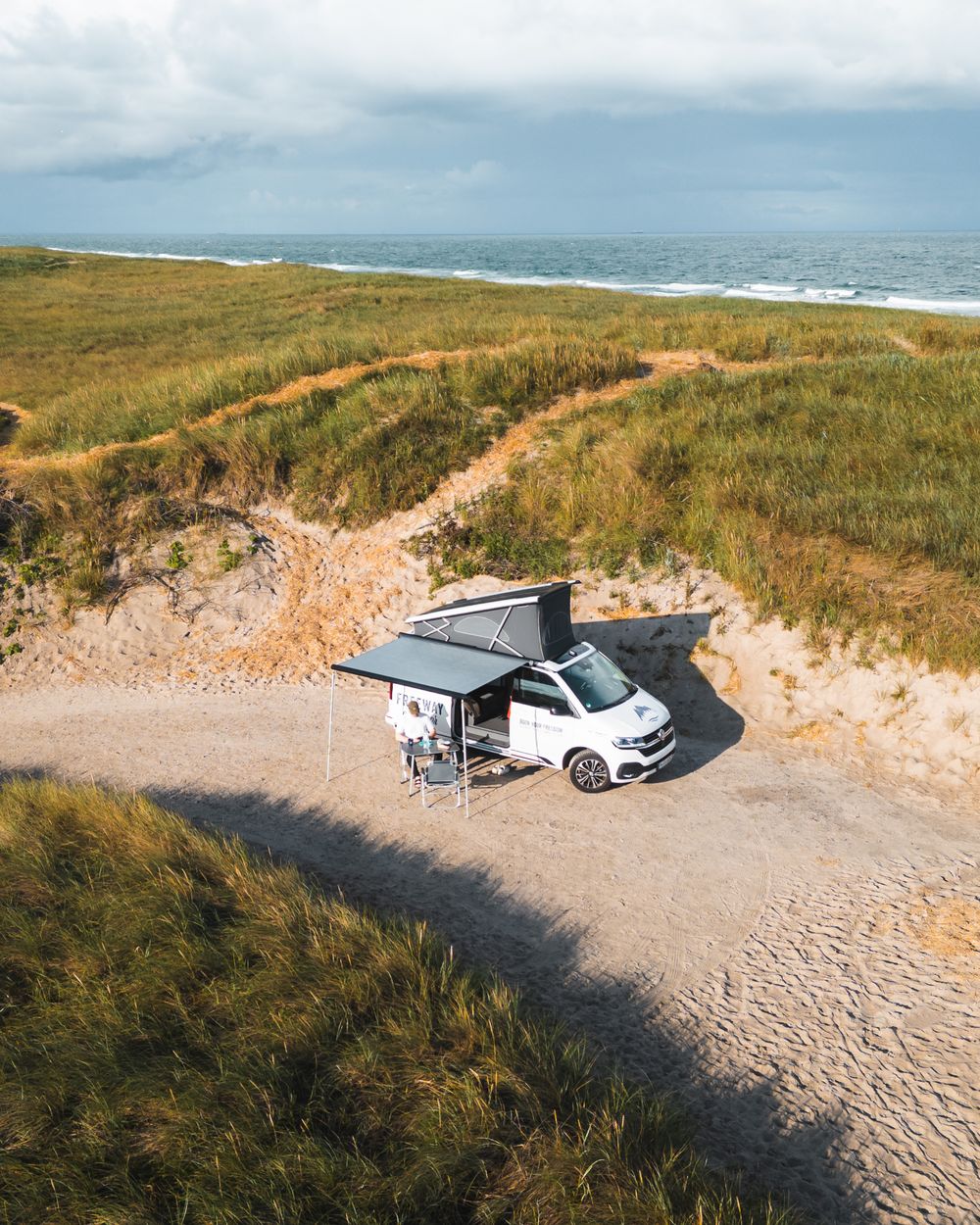 Campervan parked at an empty dune backed beach, seen from above