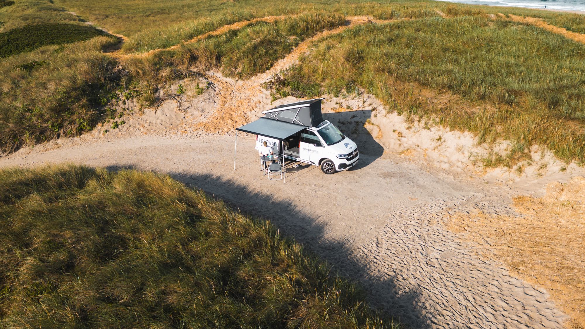 Campervan parked at an empty dune backed beach, seen from above