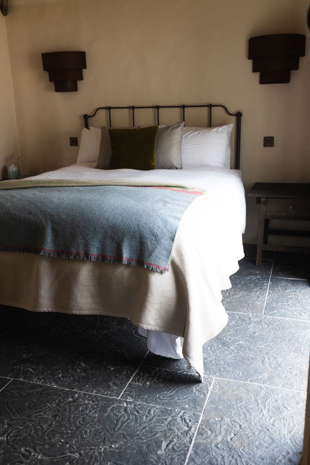 Iron framed bed with olive and sage linen on a slate floor