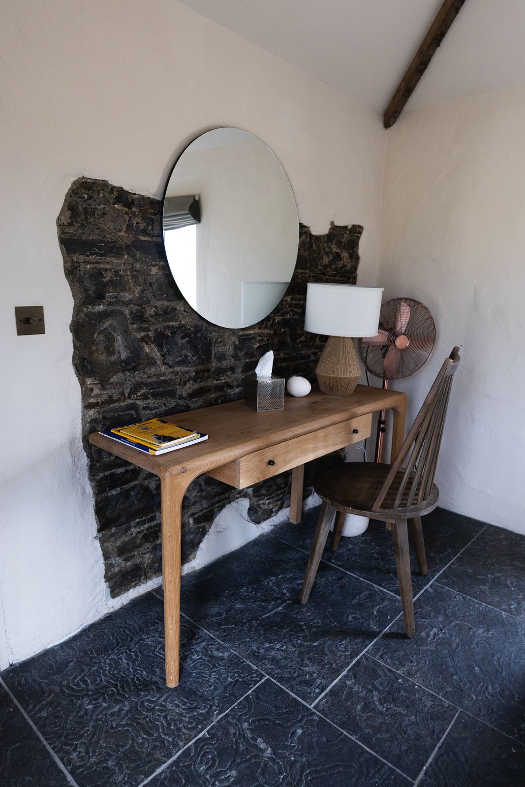 Round mirror above a writing desk against exposed stone