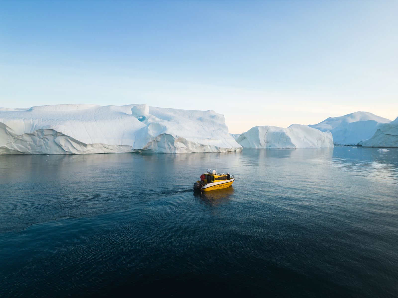 Boat reflected beside towering walls of ice