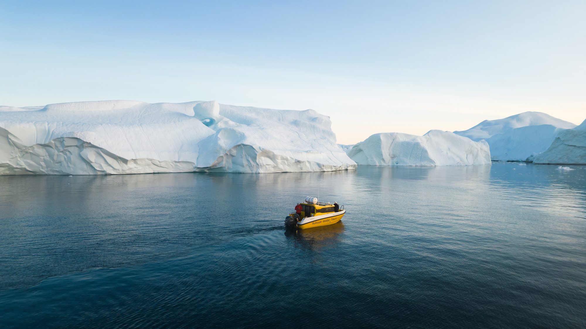 Small boat dwarfed by towering icebergs in the Ilulissat Icefjord