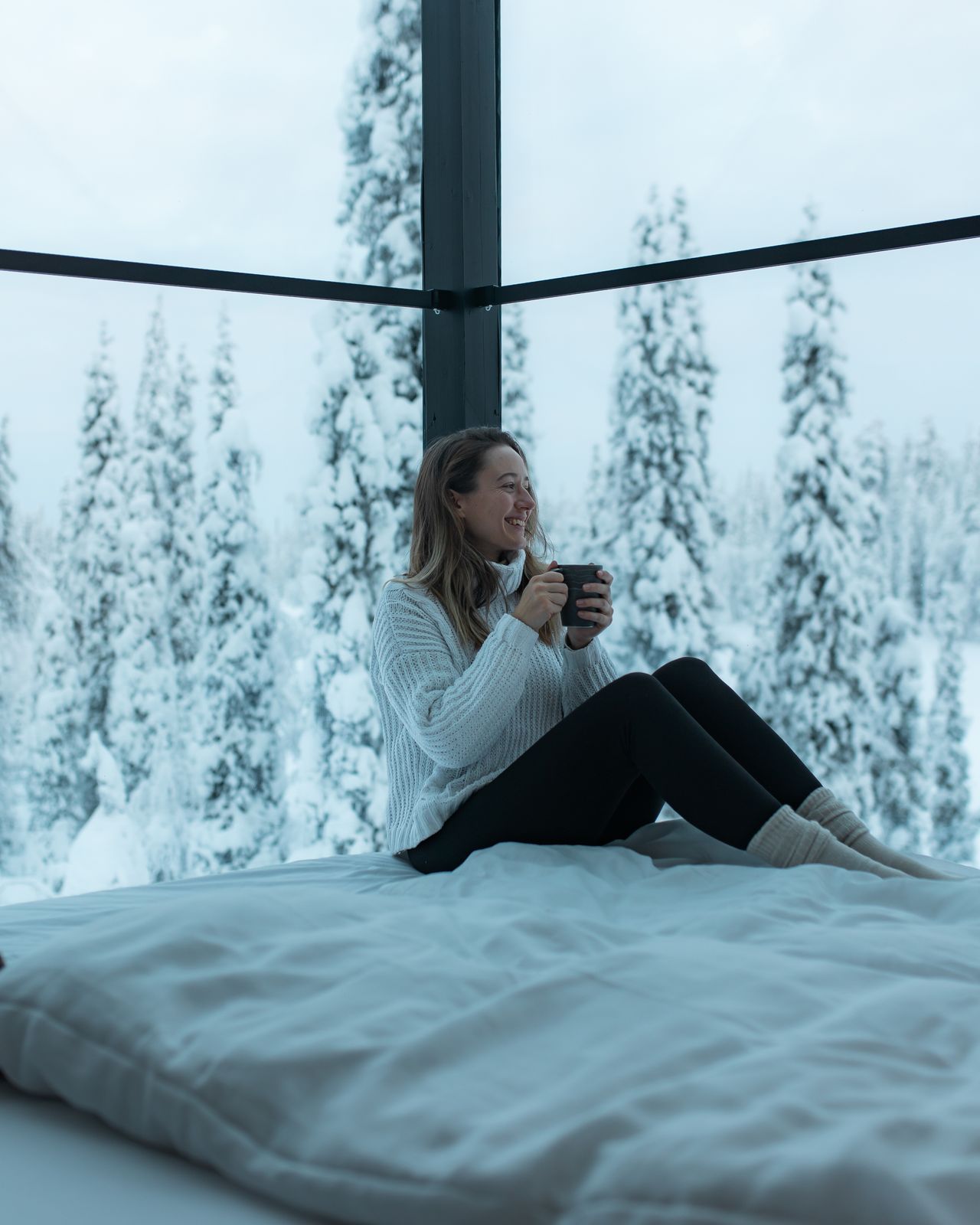 Guest with a hot drink on the bed, looking into the trees