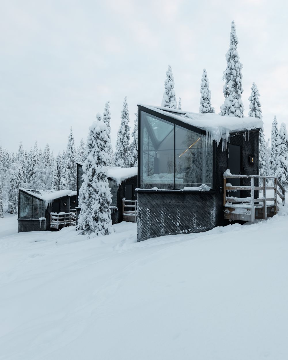 Row of glass fronted cabins in deep snow among pine trees, Finnish Lapland