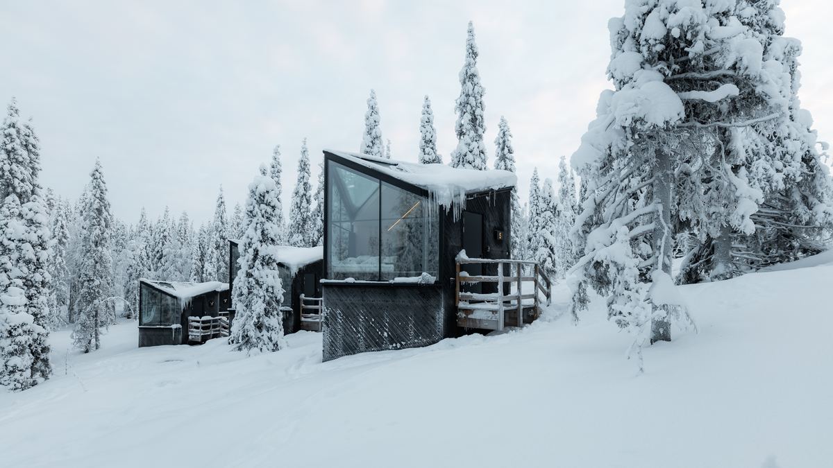Row of glass fronted cabins in deep snow among pine trees, Finnish Lapland