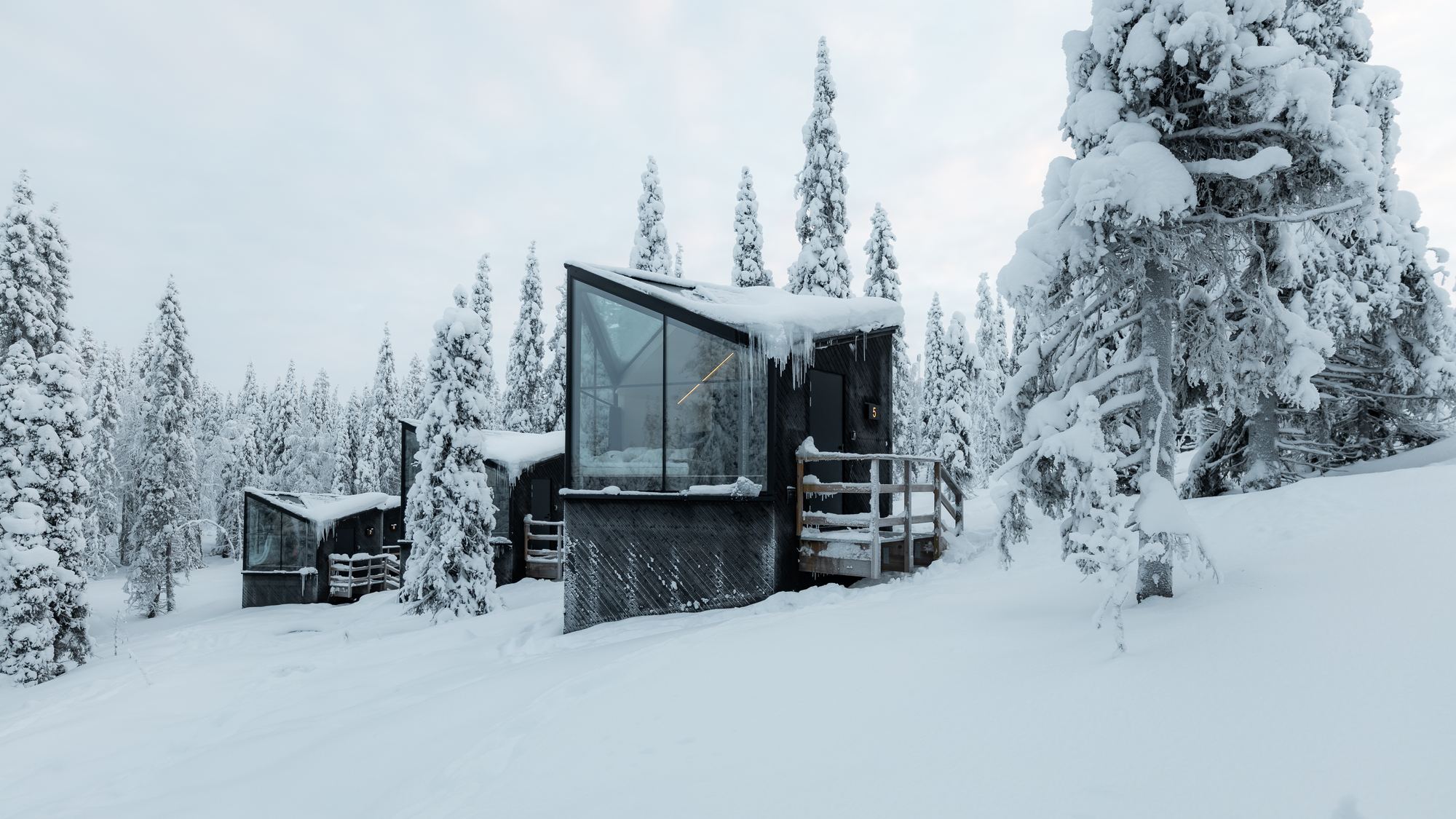 Row of glass fronted cabins in deep snow among pine trees, Finnish Lapland