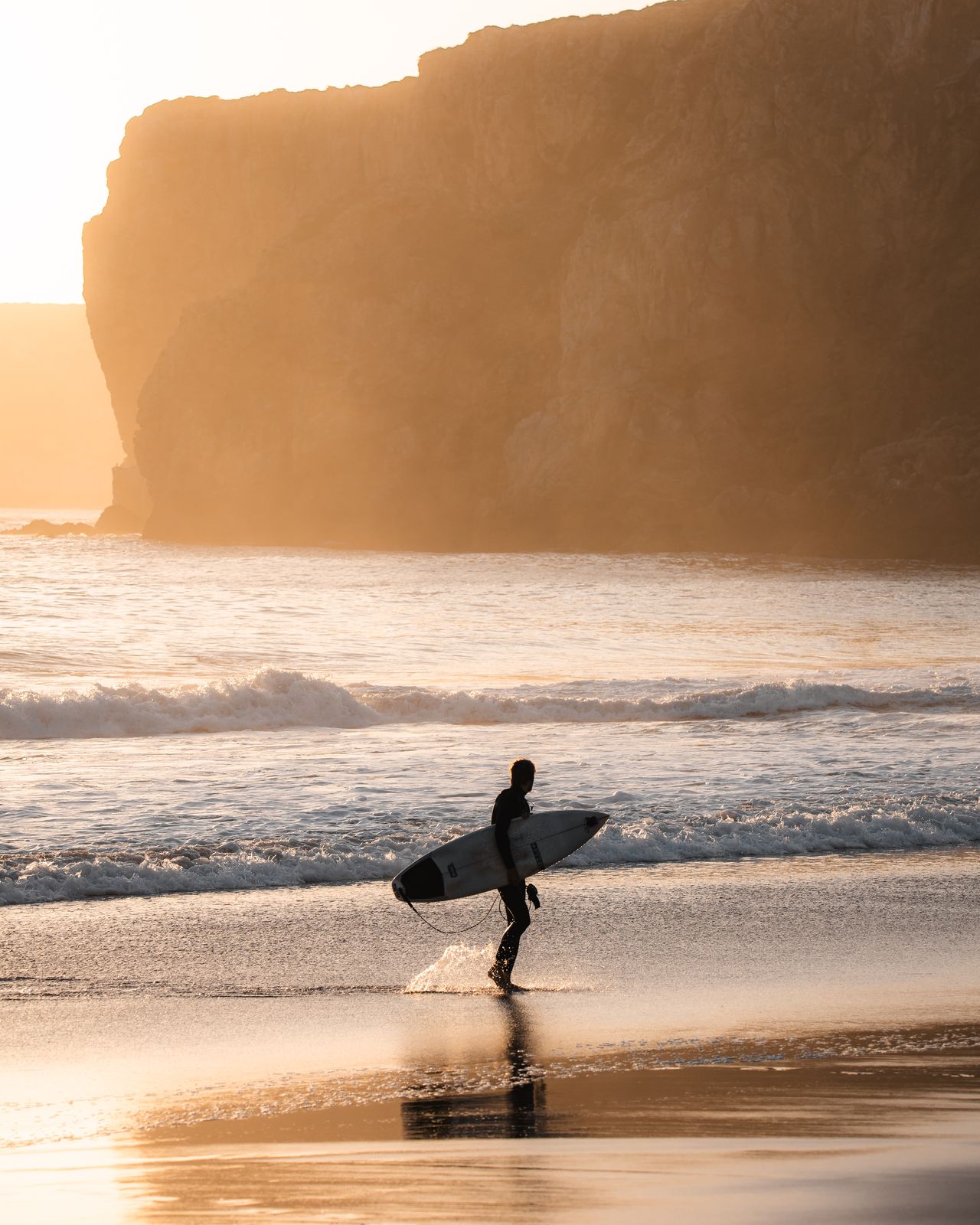 Surfer silhouetted against low sun on wet sand