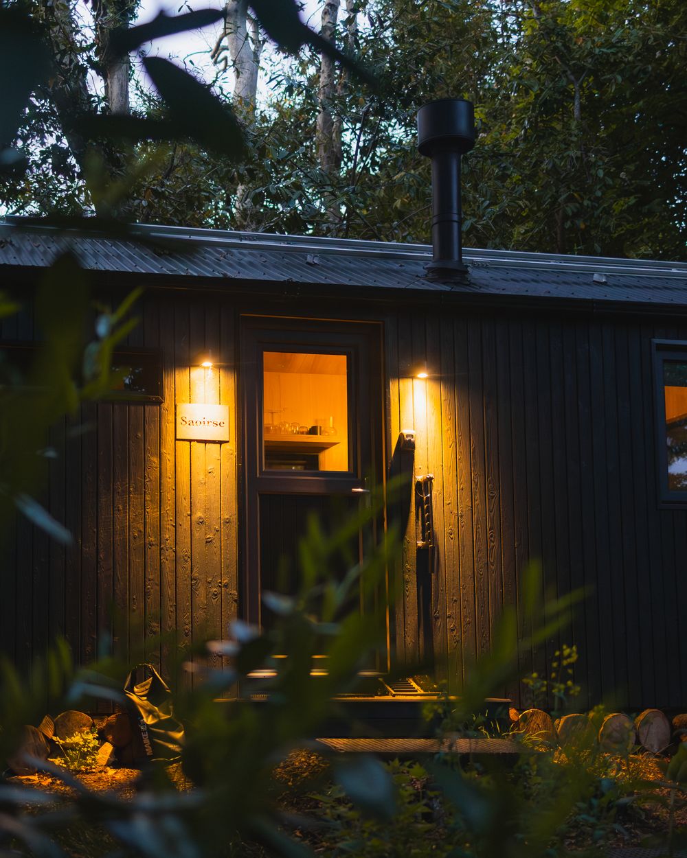 Samsu cabin lit warm at dusk in dense woodland
