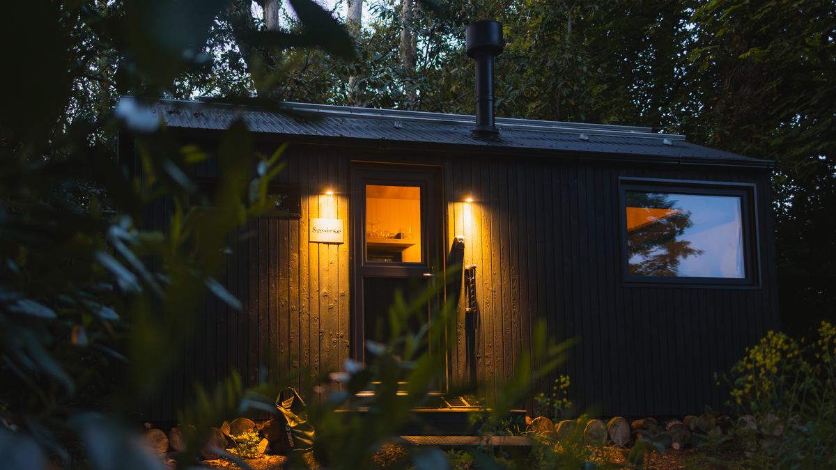 Samsu cabin lit warm at dusk in dense woodland